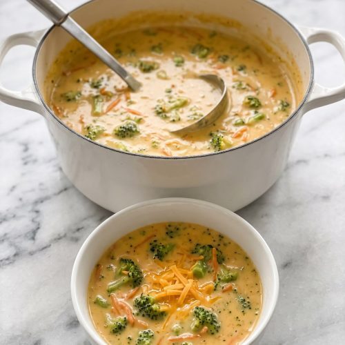 A Dutch oven of creamy golden broccoli cheddar soup with a bowl served in front