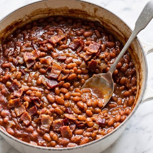 A Dutch oven of brown sugar baked beans topped with crisp chopped bacon