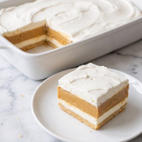 A square of layered butterscotch lush on a plate in front of the baking dish