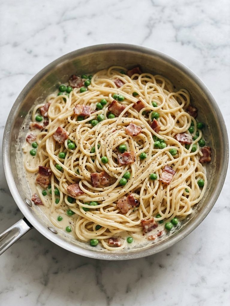 A skillet of creamy spaghetti with bacon and peas