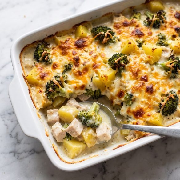 A casserole dish of chicken, broccoli and potatoes in creamy sauce with a golden cheese top, one serving scooped out