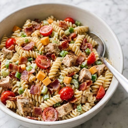 A large bowl of chicken club pasta salad with bacon, cheddar cubes, tomatoes and ranch