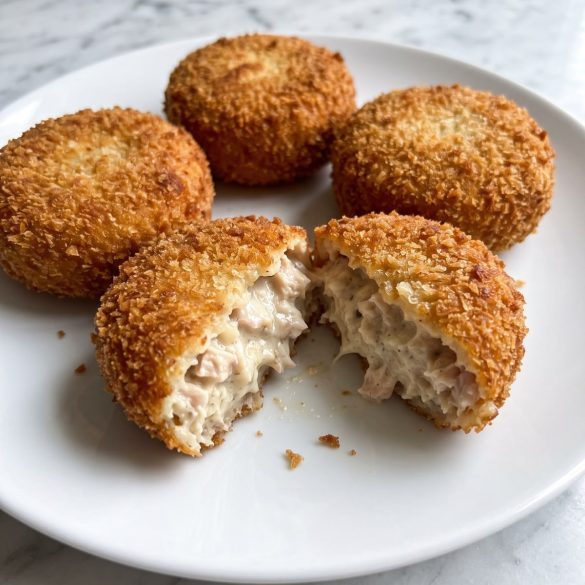 Four golden breaded chicken croquettes on a white plate, one broken open to show the creamy filling