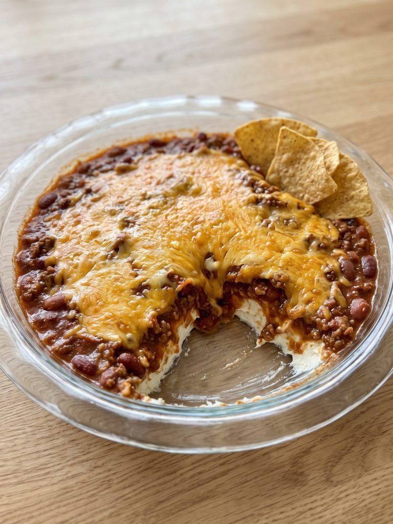 Chili dip with melted cheddar over chili and cream cheese in a glass pie dish with tortilla chips