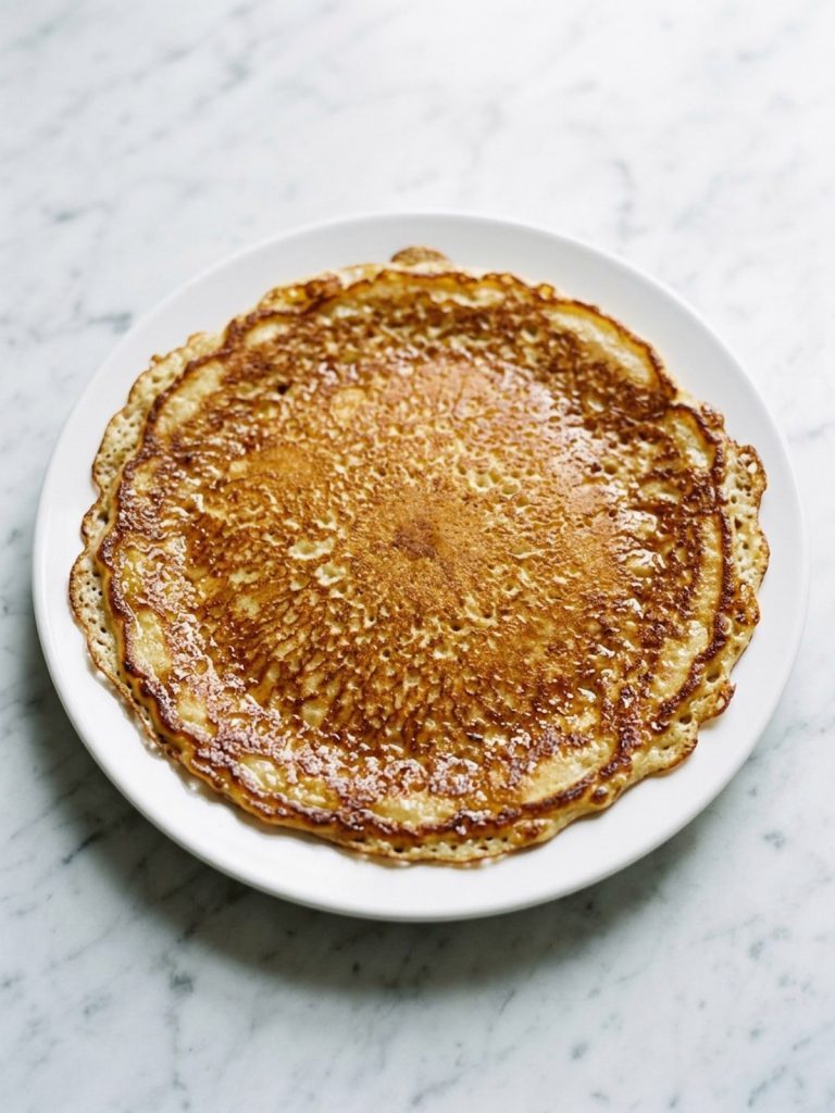 A golden buttermilk pancake with a crisp lacy edge on a white plate