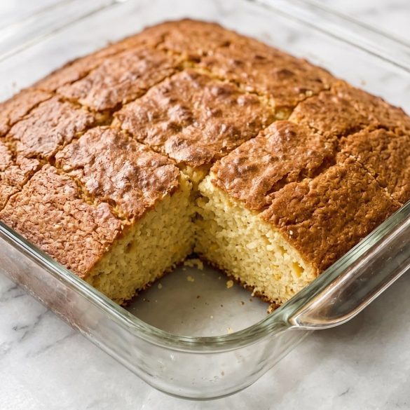 Golden creamed corn cornbread in a square baking dish, cut into squares with one piece removed