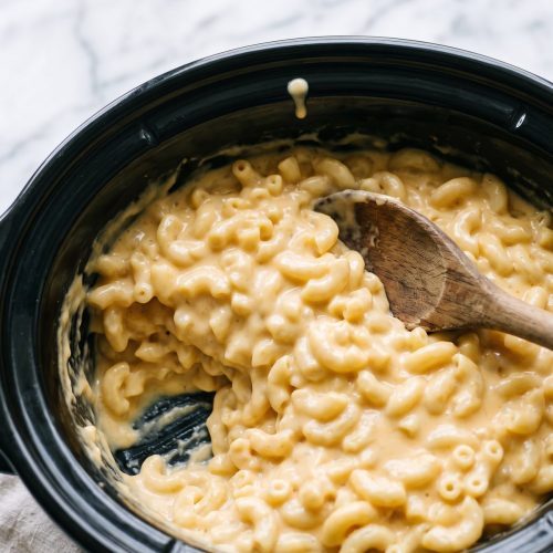 Creamy crockpot mac and cheese in a black slow cooker with a scoop taken out
