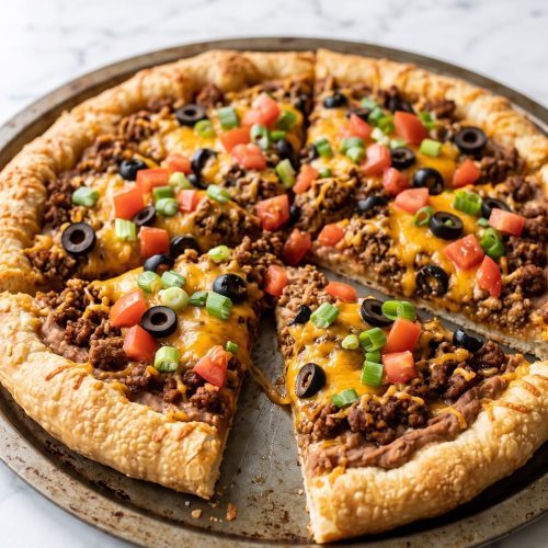 A round taco pizza with seasoned beef, melted cheddar, olives, tomatoes and green onions
