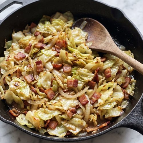 A deep skillet of fried cabbage with crisp diced bacon and onion