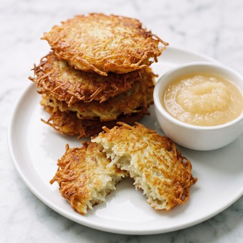 A stack of crisp golden German potato pancakes with a small bowl of applesauce
