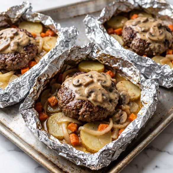 Opened hobo foil packets with ground beef patties, sliced potatoes, carrots and onion