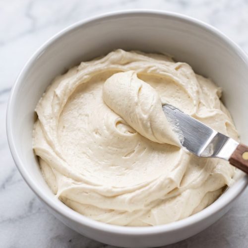 A bowl of fluffy white vanilla buttercream frosting with a spatula
