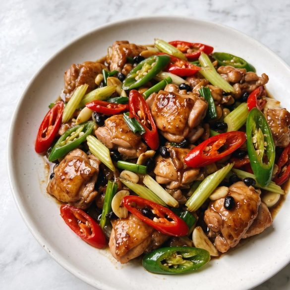 A plate of Hunan chicken stir-fry with sliced chili peppers, celery and scallions in a dark glossy sauce
