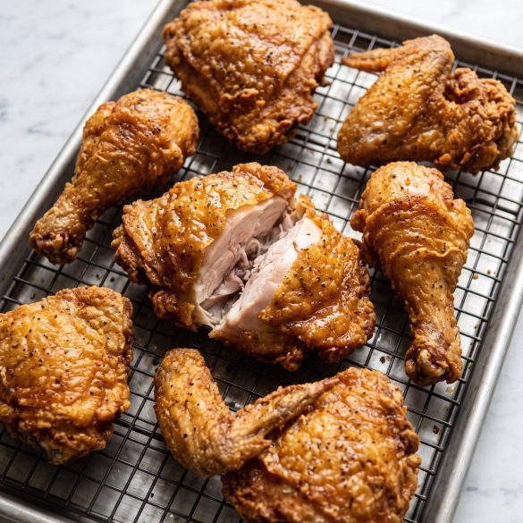 Copycat fried chicken pieces with a golden herb-speckled crust on a wire rack