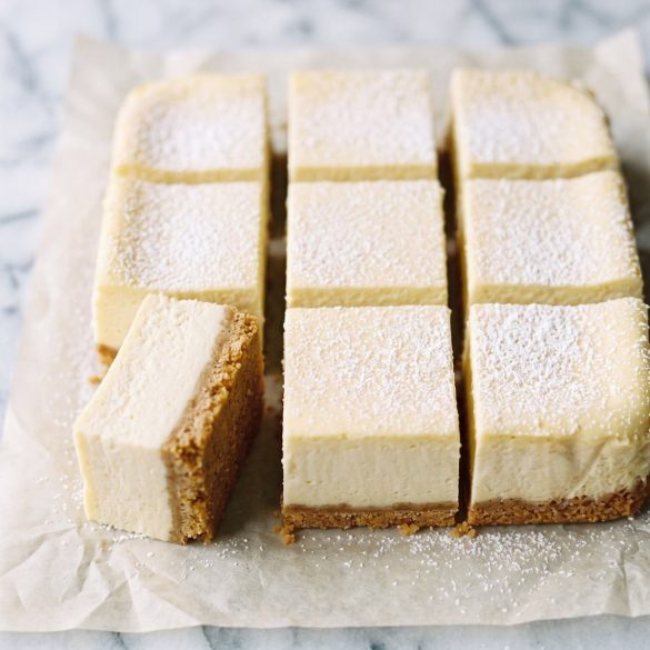 Squares of lemon cheesecake bars with a graham cracker crust, dusted with powdered sugar