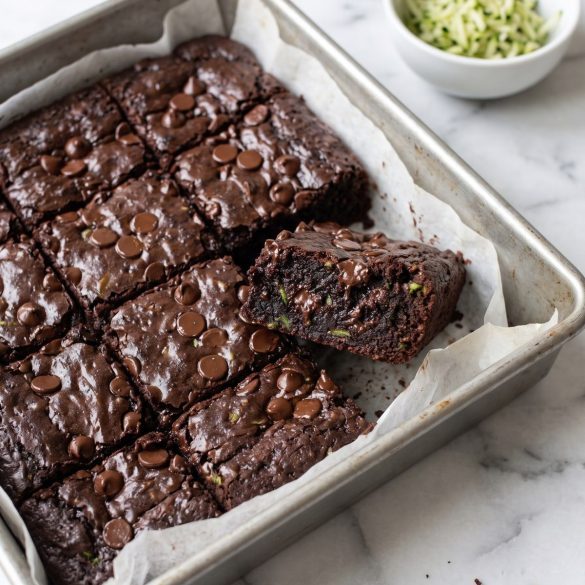 Fudgy chocolate zucchini brownies cut into squares in a parchment-lined pan, with melted chocolate chips on top
