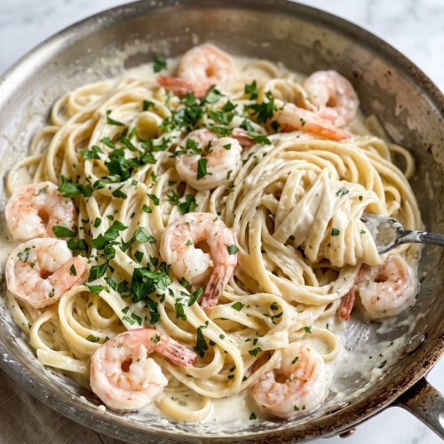 Shrimp fettuccine Alfredo in a large skillet with creamy Parmesan sauce and parsley