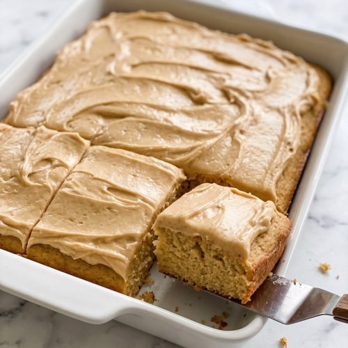 A 9x13 peanut butter cake with thick tan frosting, one square cut and lifted out