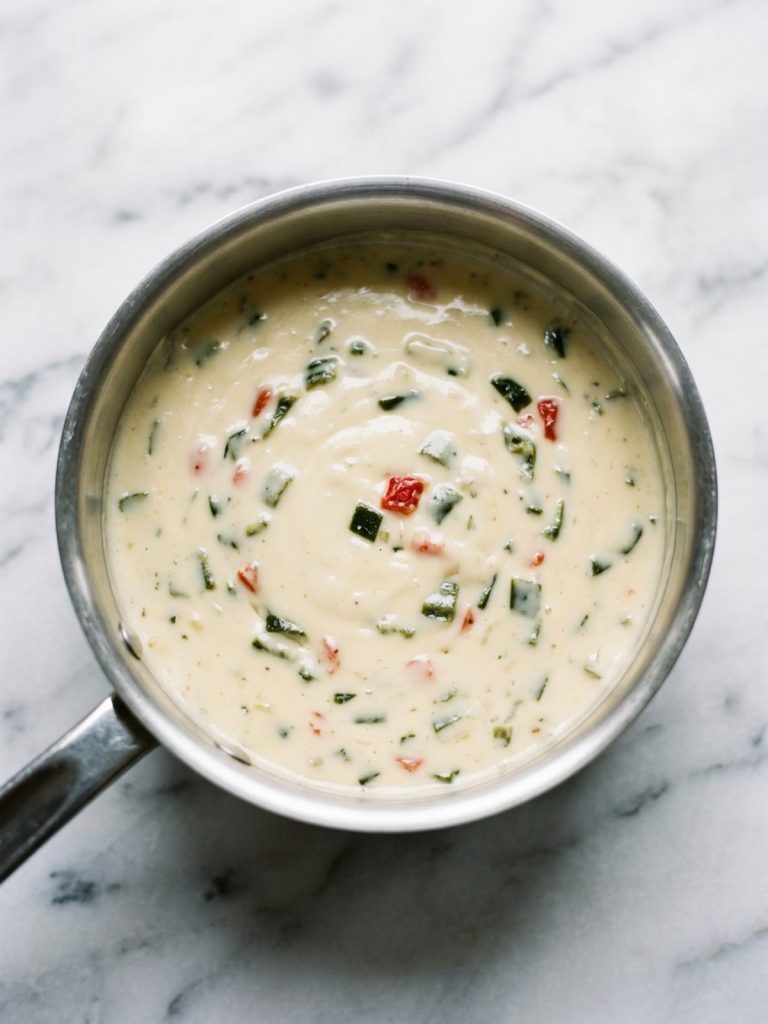 A saucepan of smooth melted three-cheese queso with poblano and tomato