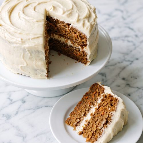 A two-layer carrot cake with cream cheese frosting and one slice cut out