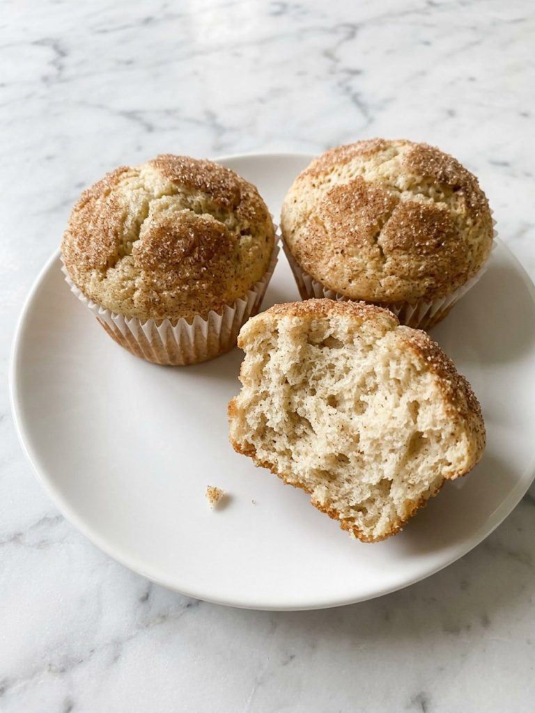 A snickerdoodle muffin with a cinnamon-sugar crust broken open to show the soft crumb