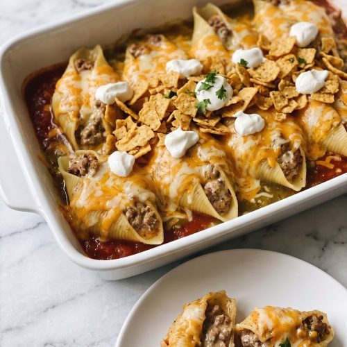 Taco stuffed shells in a baking dish with melted cheese, crushed corn chips and sour cream