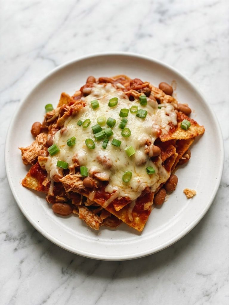 A plate of tortilla chip casserole with chicken, pinto beans, red enchilada sauce and melted cheese