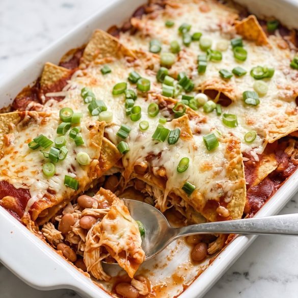 A baking dish of tortilla chip casserole with melted cheese, red sauce and green onions, one serving scooped out