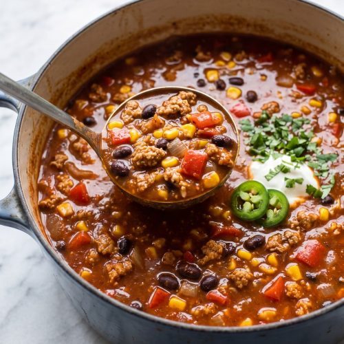 A pot of red turkey enchilada soup with black beans, corn and peppers, with a ladle