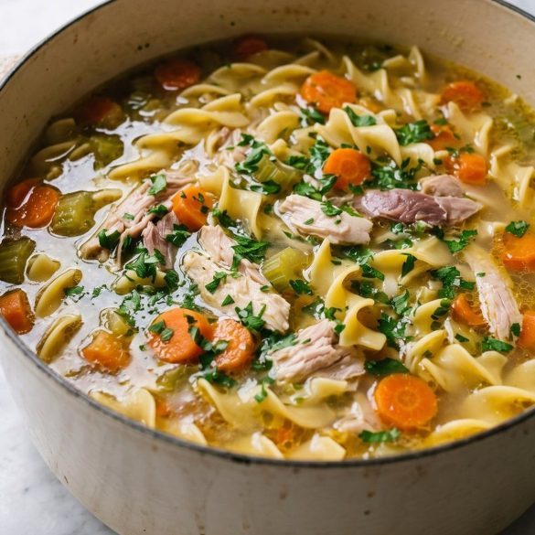 A pot of turkey noodle soup with carrots, celery, egg noodles and shredded turkey in golden broth