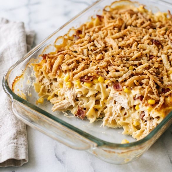 Ultimate chicken casserole in a glass baking dish with one square scooped out, showing creamy egg noodles, chicken, corn and bacon under golden French fried onions